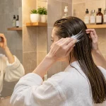 Femme aux cheveux fins et raides appliquant une mousse coiffante volumisante devant son miroir de salle de bain