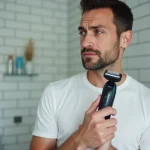 Homme examinant la tête de rasage de son rasoir Philips OneBlade dans une salle de bain moderne